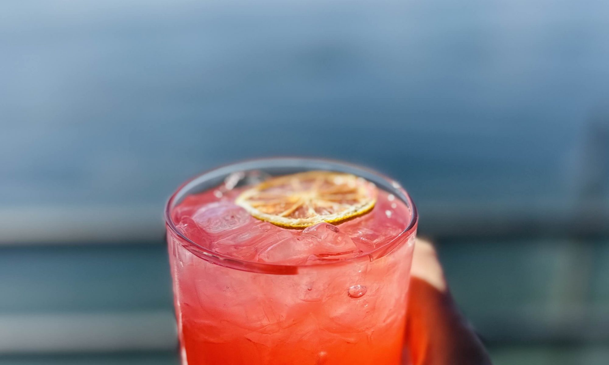 Hand holding a cocktail overlooking the water views at Ray's