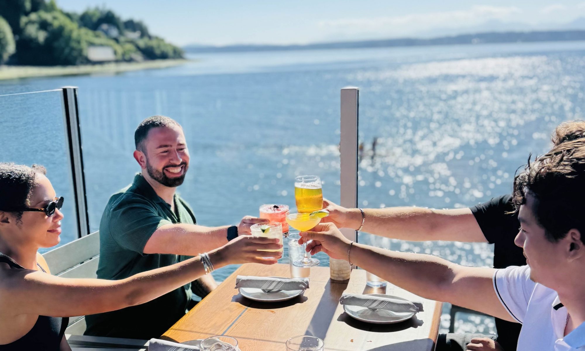Guests cheers on the outdoor deck at Ray's Boathouse on a sunny day during happy hour.