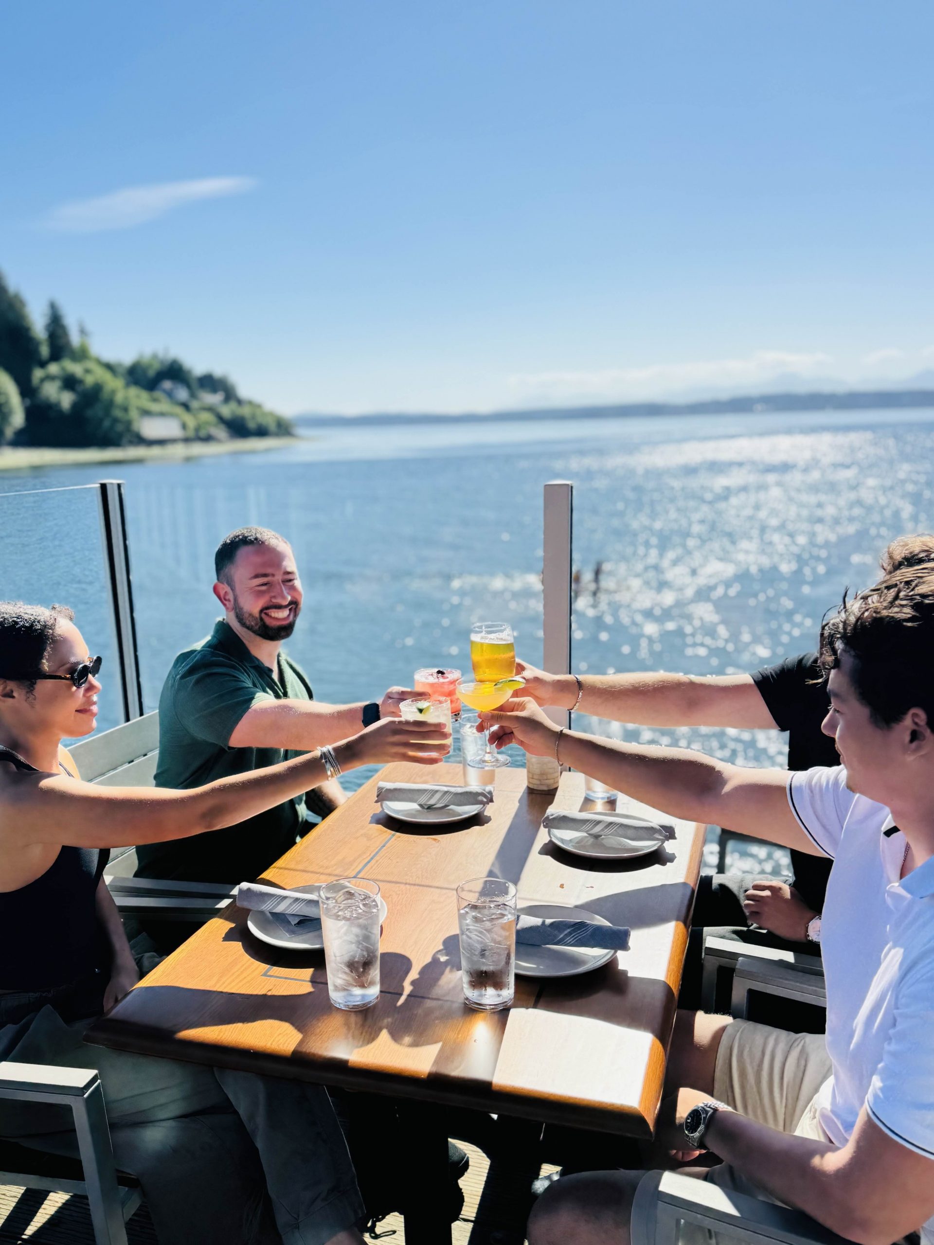 Guests cheers on the outdoor deck at Ray's Boathouse on a sunny day during happy hour.